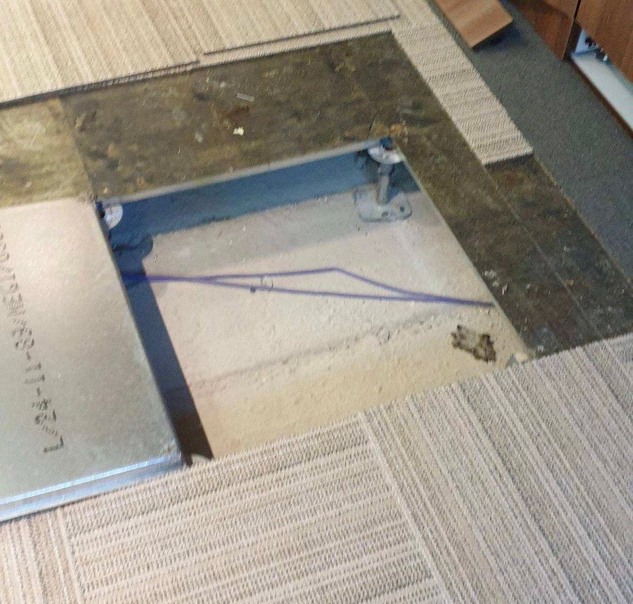 A floor tile lifted to mark out the cable route for a boardroom AV installation