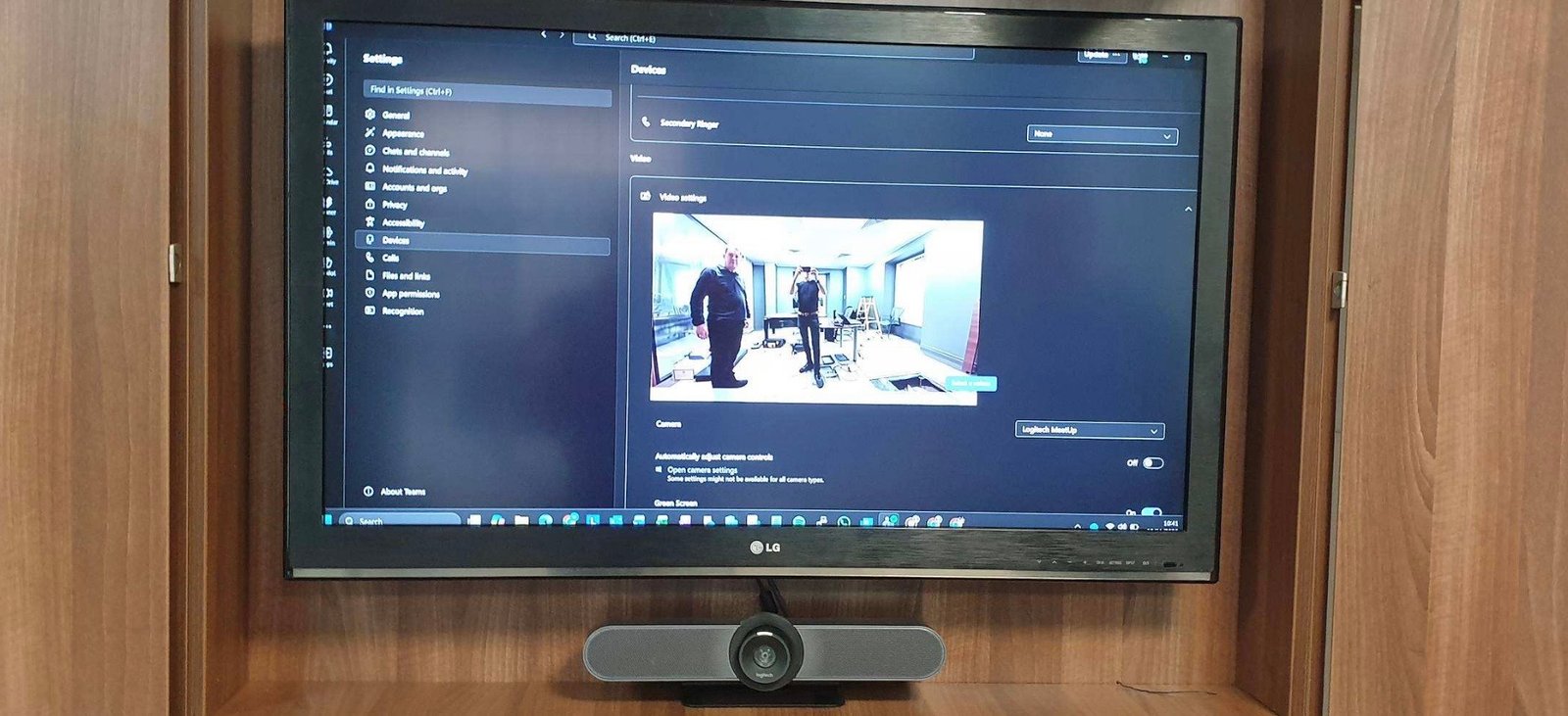 A boardroom screen running Microsoft Teams with a video-conferencing camera bar, built into the room's existing cabinetry