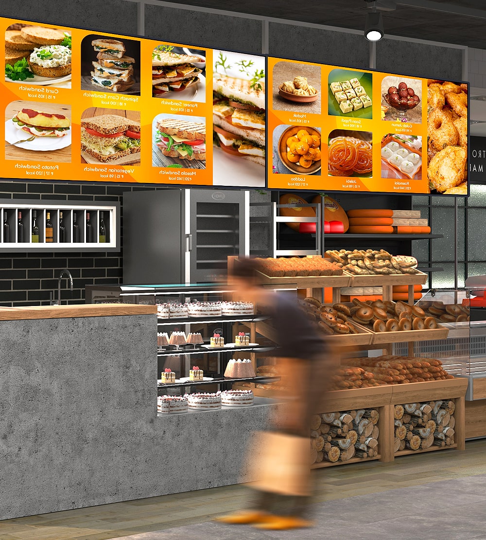 Illustrated digital menu boards above a bakery counter showing sandwiches and pastries