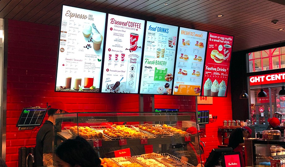 Wall-mounted digital menu boards above a café counter