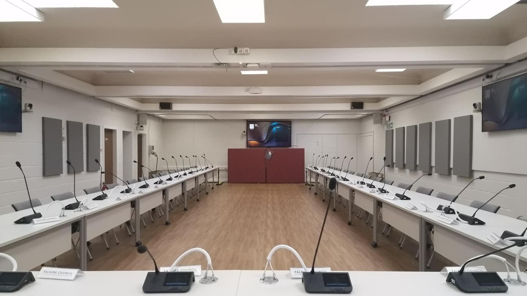 Falkirk Council Committee Chamber after its AV upgrade, showing delegate touchscreen positions running the length of both tables toward wall-mounted displays