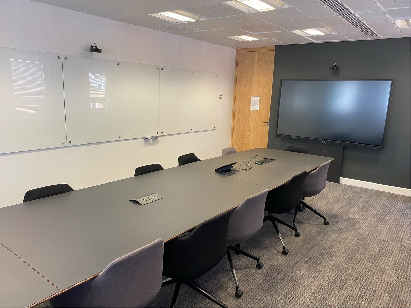NTT DATA London boardroom - the glass whiteboard wall opposite the display wall, with a further Huddly camera position above